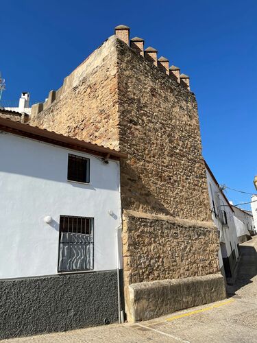 Torre medieval del frente este del recinto amurallado de Zufre con merlones modernos forrada de mampostería